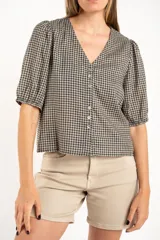 Blusa de algodón con estampado de cuadros vichy en tonos negro y blanco. Presenta escote en V, cierre frontal con botones y mangas cortas abullonadas con terminación elástica.