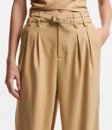 Pantalón de vestir color beige, de corte recto, con cintura alta, trabillas y cinturón cruzado. Presenta pliegues delanteros y bolsillos laterales.