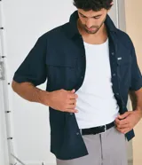 Camisa de manga corta color azul marino de corte boxy, con cuello inglés, cierre frontal de botones metálicos a presión y bolsillos cargo en el pecho.