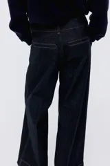 Pantalón de jean estilo wide leg, de tiro alto y corte holgado. Confeccionado en denim rígido de color azul oscuro, presenta costuras a contratono, bolsillos laterales al bies y bolsillos traseros decorativos.