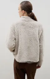 Campera de sherpa color beige con cuello alto, cierre frontal completo y bordado a contra tono en el pecho.