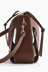 Cartera bombonera combinada de cuero sintético marrón con pespuntes blancos y bolsa interior de lona de mezcla de algodón y lino. Cuenta con diseño estructurado, cierre ajustable con cordón y correa bandolera extraíble con mosquetones metálicos dorados.
