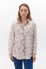 Camisa de manga larga con cuello clásico y cierre frontal de botones, confeccionada en tela con estampado floral en tonos chocolate sobre fondo beige.