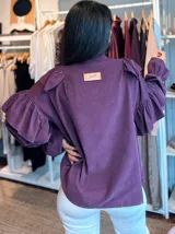 Camisa de pana fina color azul, con diseño de volados en los hombros y mangas largas abullonadas con puños elásticos. Presenta cierre frontal con botones y cuello con detalle de volado.