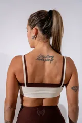 Top deportivo de doble capa en color crema con detalles en marrón oscuro, con breteles finos y logo bordado en el centro del pecho.