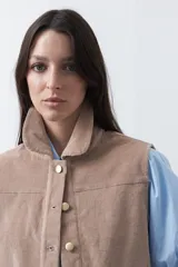 Chaleco de pana color marrón oscuro, con cuello camisero, cierre frontal de botones metálicos dorados y dos bolsillos frontales con detalle de bordado geométrico.