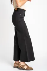 Jean de corte wide leg y tiro medio, confeccionado en algodón peinado de color negro. Presenta un diseño de pierna ancha con ruedo deshilachado y cierre frontal con botón y cremallera.