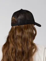 Gorro trucker negro de cinco paneles con malla en la parte trasera, visera curva y parche frontal redondo con el logo de Cat en amarillo.