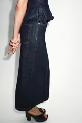 Falda midi de tiro alto confeccionada en denim oscuro, con cinco bolsillos estilo jean, cierre frontal con cremallera y botón, y abertura en la espalda. Presenta pespuntes en color rojo contrastante.
