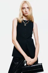 Chaleco largo negro con cuello redondo y cierre de botones frontales. Diseño entallado con bolsillos delanteros ribeteados y abertura en la parte trasera.