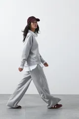 Pantalón de corte holgado y pierna ancha, con cintura elástica ajustable mediante cordón. Presenta bolsillos laterales y costuras verticales decorativas que recorren el frente de las piernas.