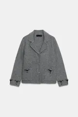Chaqueta de punto gris con cuello solapa, manga larga y cierre frontal con botones forrados. Presenta bolsillos delanteros de plastrón y detalles de abalorios joya en los bolsillos y en los puños.