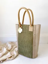 Bolso matero verde con textura croco y detalles en beige. Tiene doble asa corta y accesorio metálico en forma de cruz.