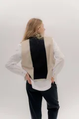 Chaleco abierto de tejido de punto, con diseño de bloques de color verticales en gris claro, negro y gris oscuro. Presenta un cuello ancho tipo chal y un detalle de tres pequeñas aplicaciones bordadas horizontales en tonos verde oliva, naranja quemado y celeste pálido en el frente.