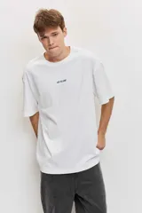 Remera blanca de manga corta, corte oversize, con estampa en la espalda de una flor sobre fondo difuminado verde y blanco.