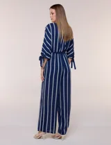 Enterito largo de crepe color azul marino con diseño de rayas verticales blancas. Cuenta con escote redondo, mangas tres cuartos con detalles de lazos en los puños, cintura elastizada con lazo extraíble para ajustar, bolsillos laterales y pantalón de corte amplio.