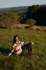 Sweater de punto con diseño de rombos en tonos marrones, beige y crema. Presenta cuello redondo, mangas largas con puños anchos acanalados y diseño de rayas en los puños y el ruedo.