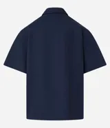 Camisa de manga corta color azul marino de corte boxy, con cuello inglés, cierre frontal de botones metálicos a presión y bolsillos cargo en el pecho.