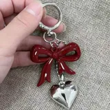 Llavero con aro metálico plateado, dije de lazo rojo brillante y dije de corazón plateado.