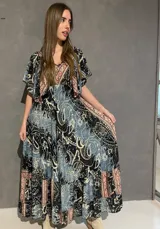 Vestido largo con escote en V tanto en el frente como en la espalda, mangas cortas amplias y corte elastizado debajo del busto. Presenta un estampado de estilo paisley y guardas geométricas en tonos azules, negros y corales.