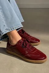 Championes de cuero vacuno con acabado charolado en color bordó, con cordones al tono y suela de goma color caramelo.