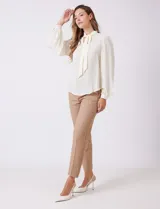 Blusa de gasa color crema, marca Zac & Rachel, con escote en V y lazo para anudar en el cuello. Mangas largas con puños abotonados.