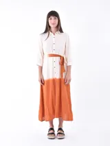 Vestido midi color crudo con efecto degradado color naranja en la parte inferior. Tiene corte camisero, cuello clásico, mangas 3/4 y cinturón de tela color naranja.