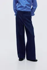 Pantalón de jean tipo wide leg de tiro alto, confeccionado en denim rígido de color azul oscuro. Presenta un corte holgado desde el muslo hasta el ruedo, con raya marcada en el centro de las piernas, cierre con botón oculto y bolsillos al bies.