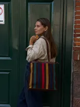 Cartera tipo tote de cuero con diseño de franjas verticales multicolores en tonos tierra, rojo y azul. Cuenta con correas trenzadas de cuero y cierre superior.