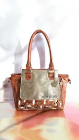 Cartera de cuero color marrón terra y dorado, con solapa de cuero texturizado, arte pintado a mano en la base, doble asa de hombro y herrajes metálicos.