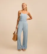 Enterito largo de jeans celeste, con breteles finos, escote recto, bolsillos delanteros y traseros, y trabillas en la cintura.