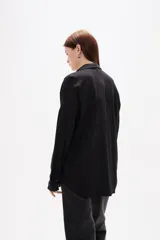 Camisa de corte holgado con estampado de rayas verticales en tonos bordó y blanco. Presenta cuello clásico, cierre frontal con botones, mangas largas con puños abotonados y un bolsillo frontal en el pecho.