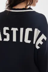 Cardigan de punto negro con diseño estilo varsity, escote en V y cierre frontal de botones. Presenta líneas blancas en contraste a lo largo de la botonera, el escote, los puños y el ruedo.