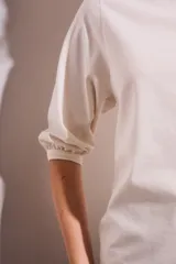 Remera de algodón color blanco roto, con escote redondo y mangas globo de tres cuartos con elástico en el puño.