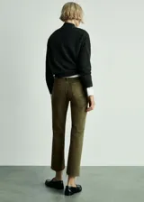 Pantalón tipo jeans de tiro medio en color verde oliva, con diseño acampanado y bajo deshilachado. Presenta dos bolsillos de parche en la parte delantera, cierre de cremallera y botón, y trabillas para cinturón.