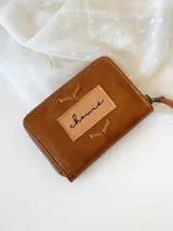 Billetera pequeña de cuero color marrón con cierre metálico y diseño de espiga. Incluye monedero interno.
