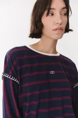 Remera de manga larga con diseño a rayas horizontales en azul marino y bordó. Presenta cuello redondo en color crema, logo bordado en el centro del pecho y costuras decorativas hechas a mano en color crema en la unión de las mangas.