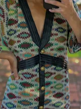 Vestido midi de silueta recta, con escote en V profundo y cuello camisero en contraste. Presenta cierre frontal con botones, mangas largas con leve volumen y tajos laterales. Diseño versátil que puede utilizarse como vestido o como camisero.