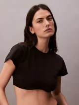 Remera cropped de algodón con corte boxy, cuello redondo y mangas cortas. Presenta un bajo redondeado en la parte delantera y un diseño con espalda abierta y lazo decorativo.