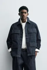 Chaqueta de denim de algodón en color azul oscuro, con corte relajado, cuello solapa, manga larga y cuatro bolsillos frontales con solapa. Presenta cierre frontal oculto por solapa.