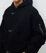 Campera de sarga de algodón con capucha, cierre frontal con cremallera y trabas metálicas decorativas. Presenta un bolsillo con cierre en la manga y puños elásticos, con un diseño de estilo utilitario.