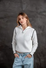 Buzo de punto color blanco con cuello polo y cierre frontal. Presenta detalles de rayas negras en los hombros y puños, con un diseño de tejido acanalado.