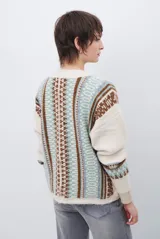 Cardigan de punto con escote en V y cierre frontal de botones. Presenta un diseño estampado con patrones geométricos en tonos beige, marrón y detalles en azul vibrante.
