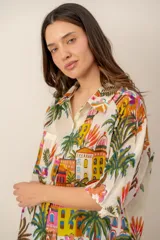 Camisa oversize de lino color crudo, con cuello camisero y estampado multicolor de paisajes tropicales con palmeras y arquitectura.