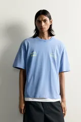 Camiseta relaxed fit de color celeste con efecto acid wash, cuello redondo y manga corta. Cuenta con estampa frontal con la inscripción "HOTEL STAFF" y "Escape Ibiza" en tonos amarillos.