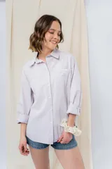 Camisa verde pastel de algodón, corte oversize, con cuello camisero, cierre con botones, mangas largas con puños con volados de encaje blanco, dos bolsillos frontales con solapa y ruedo irregular. 