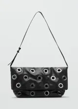 Bolso tipo tote de color negro, confeccionado en poliuretano, con diseño de ojales metálicos plateados distribuidos por toda la superficie y asas largas para llevar al hombro.