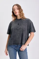 Remera de manga corta con efecto lavado oscuro (acid wash), corte holgado y un pequeño bordado de estrella o brújula en el centro del pecho.