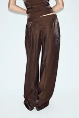 Pantalón de tiro alto color marrón con tejido de efecto brillo y pernera recta. Cuenta con bolsillos delanteros y cierre frontal con cremallera, botón interior y gancho.
