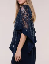 Vestido largo azul marino de seda fría, compuesto por una falda recta con tajo frontal y una capa superior superpuesta de encaje con lentejuelas bordadas, escote a la base y mangas tres cuartos acampanadas.